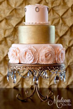 a three tiered wedding cake with pink roses on the top and gold trimmings