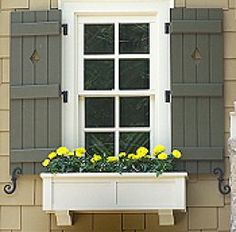 a window with shutters and yellow flowers in the window sill on a building