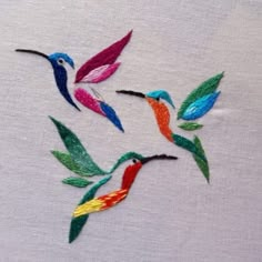 three embroidered hummingbirds on white fabric with green, red and blue feathers flying in the air