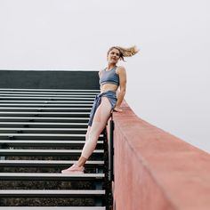 a woman standing on top of a metal rail next to a red wall with her hair blowing in the wind