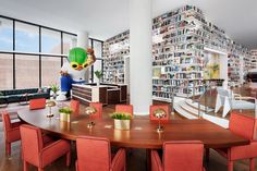 a dining room table with red chairs and bookshelves on the wall behind it