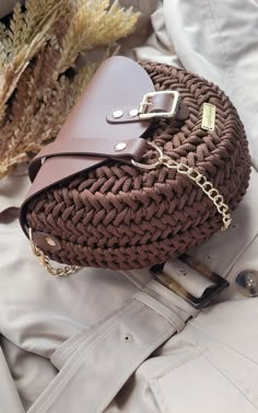 a brown purse sitting on top of a bed next to a white pillow and some dried plants