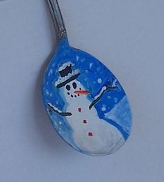 a spoon with a painted snowman on it is hanging from the side of a wall