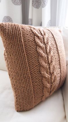 a brown knitted pillow sitting on top of a white couch next to a window