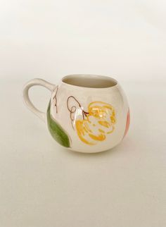 a white cup with oranges and leaves painted on it