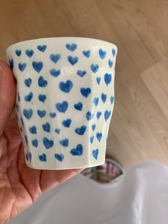 a hand holding a blue and white cup with hearts on it