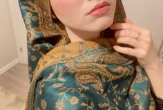 a woman in a blue and gold shawl is holding her hand on her ear