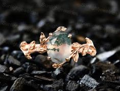 a green and white ring sitting on top of some black rocks with leaves around it