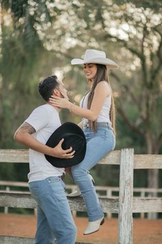 a man sitting on top of a wooden fence next to a woman wearing a cowboy hat