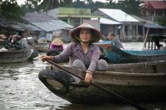 a woman sitting on top of a wooden boat in the middle of a body of water