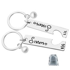 two silver key chains with the words sister and son engraved on them, sitting next to a bag