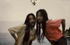 two young women standing next to each other near the ocean