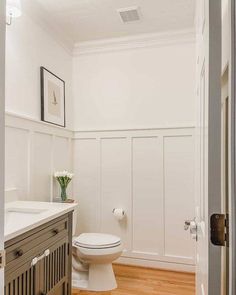 a white toilet sitting in a bathroom next to a wooden cabinet and sink under a mirror