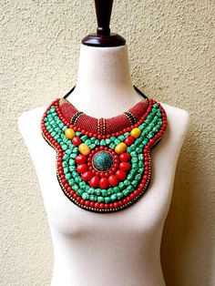 "Striking Tibetan turquoise and coral bib collar necklace in faux teal green turquoise, coral beads, with a stunning central brass medallion. Perfect with a flowing caftan or an itsy black bikini. Perfect anywhere you are barefoot! Wear your hair up, with a bright ribbon or turban, or wear it down! You don't need much else! Eye-catching geometric pattern with a mix of smooth and textured beads. This is a handmade reproduction of a Tibetan tribal neck piece or Skeypuk, which is worn as collars on Bohemian Turquoise Bib Necklace With Colorful Beads, Handmade Turquoise Bohemian Bib Necklace, Red Bohemian Bib Necklace For Festivals, Bohemian Red Bib Necklace With Round Beads, Green Bohemian Beaded Necklaces, Red Beaded Bohemian Bib Necklaces, Bohemian Bib Necklace With Colorful Beads, Green Turquoise Necklace With Colorful Beads For Festivals, Bohemian Beaded Necklaces With Round Beads