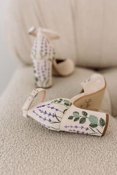 white shoes with flowers painted on them sitting on a couch next to a stuffed animal