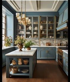 a kitchen with blue cabinets and marble counter tops, an island in the middle is surrounded by potted plants