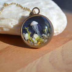 a necklace with an image of a jellyfish and seaweed in it on a wooden surface