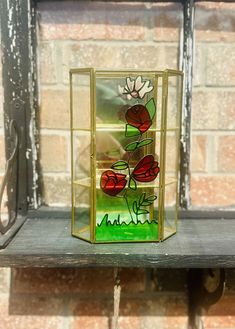 a glass vase with flowers in it sitting on a shelf next to a brick wall