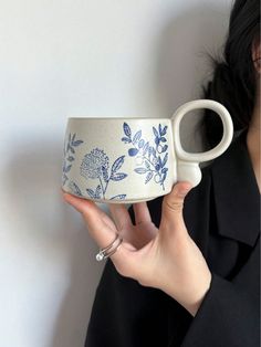 a woman holding up a white and blue coffee cup with flowers on the inside, in front of a white wall