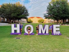 three people standing in front of a sign that says home on the grass with trees behind them