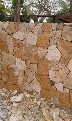 a stone wall made out of rocks with a wooden fence in the background and trees behind it