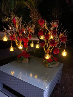 two vases with roses are sitting on a table in the dark, lit up by candles