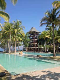 an outdoor swimming pool surrounded by palm trees and water features a gazebo in the background