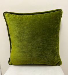 a green velvet pillow sitting on top of a white chair in front of a wall