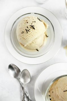 two plates with ice cream and spoons next to each other on a white table