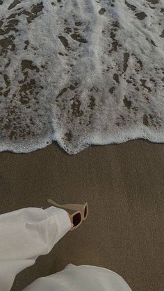 someone's feet sticking out of the sand at the beach with waves coming in