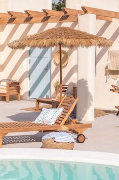 an umbrella and some chairs next to a pool with a blue door in the background