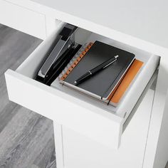 a desk with a pen, notebook and phone in it on top of a drawer