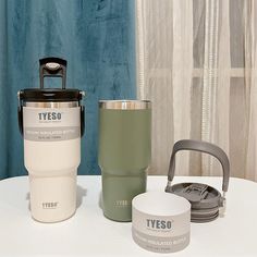 three different types of travel mugs sitting on a white table next to each other