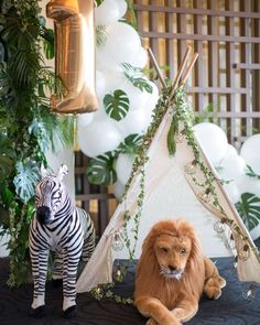 two stuffed animals are sitting in front of a teepee tent and balloon arch with greenery