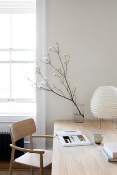 a wooden table topped with a vase filled with white flowers next to a chair and lamp