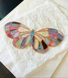 a stained glass butterfly brooch sitting on top of a piece of white tissue paper