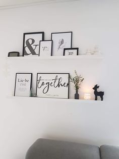 two white shelves with black and white framed pictures on them above a gray couch in a living room