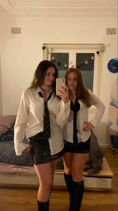 two young women dressed in short skirts and ties taking a selfie with their cell phone