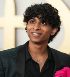 a close up of a person wearing a black suit and pink flower in his lapel