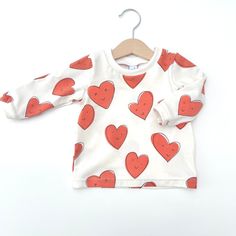 Super Cute fun heart printed t-shirt.  Available in a choice of long or short sleeves from sizes 0-3 months up to age 5-6years Our long sleeved T shirts are made of our usual super soft light fabric and are finished with cute little cuffs and a double stitched hem; perfect for layering under rompers or mix and matching with our leggings. Pattern placement may be different to that shown. Coordinating leggings, romper, hats and bibs also available. Sizing runs true to size with a relaxed fit.  See Photos for Sizing. We understand every little person is unique so if you would like to request custom sizing please just pop a note the 'add an optional note to seller' box.  Most items are made to order so please allow up to 7 days for them to be shipped.  If you need an order in a hurry get in to Playful Tops With Funny Print For Playtime, Playful Organic Cotton Tops For Playwear, Red Organic Cotton Crew Neck Top, Unisex Printed White Tops, Unisex White Printed Tops, Playful Organic Cotton Tops For Playtime, Printed Cotton T-shirt For Playtime, Red Long Sleeve Printed T-shirt, Red Printed Long Sleeve T-shirt