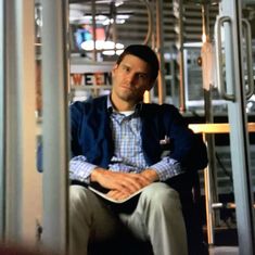 a man is sitting on a bus looking at the camera while reading a book in front of him