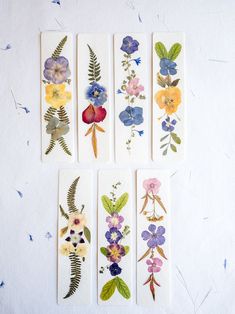 four flower bookmarks with different colors and designs on white paper, sitting on a table