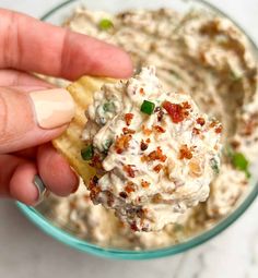 a hand holding a cracker over a bowl of dip