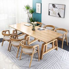 a dining room table with chairs and a plant on the wall next to it in front of a window