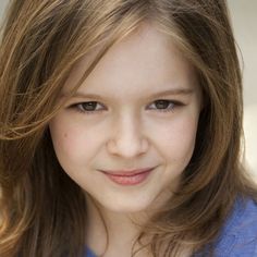 a close up of a person with long hair and blue shirt smiling at the camera