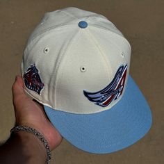 a hand holding a white and blue baseball cap with wings on it's peak