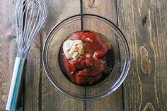 a glass bowl filled with food next to a whisk on top of a wooden table