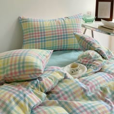 an unmade bed with plaid comforter and pillows on the bottom, next to a small side table