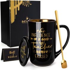 a black coffee mug with gold lettering on it and a matching spoon in front of the box