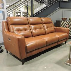 a brown leather couch sitting on top of a hard wood floor next to a stair case